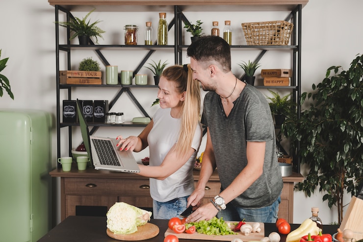 Foto gratuito mujer que muestra la computadora portátil a su marido que corta verduras en la cocina