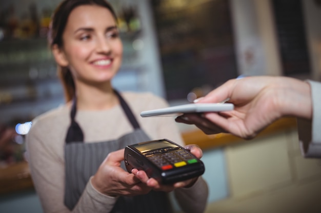 Mujer que paga la factura a través de teléfonos inteligentes usando la tecnología NFC