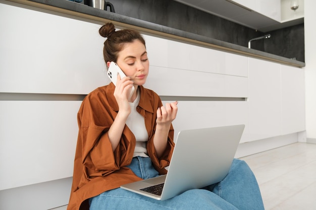 Mujer que parece aburrida y sin diversión mientras está sentada en el suelo y escuchando una conversación tiene la computadora portátil encendida