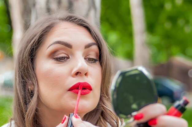 Mujer que pone, corrigiendo el lápiz labial rojo brillo de labios. Hermosa mujer morena con estilo correcto maquillaje