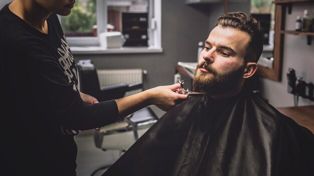 Mujer que prepara la barba del cliente con las tijeras