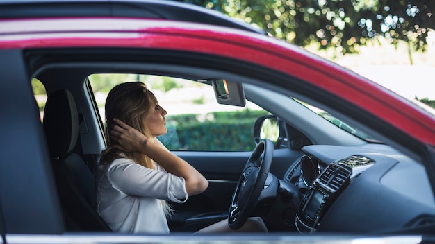 Mujer que prepara su pelo que mira el espejo retrovisor en un coche