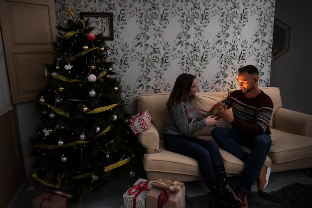 Foto gratuita mujer que presenta el paquete de regalo al hombre en el sofá cerca del árbol de navidad en la habitación