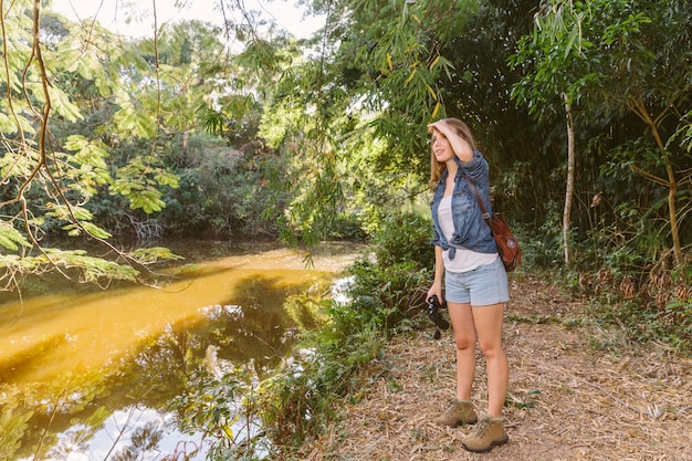 Mujer que protege sus ojos de pie junto al río en el bosque