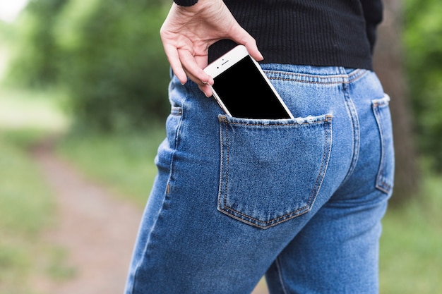 Mujer que quita smartphone del bolsillo de los tejanos