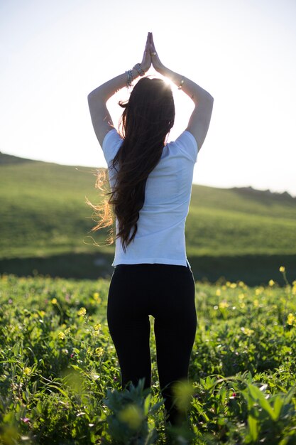 Mujer que se relaja con las manos para arriba en campo verde