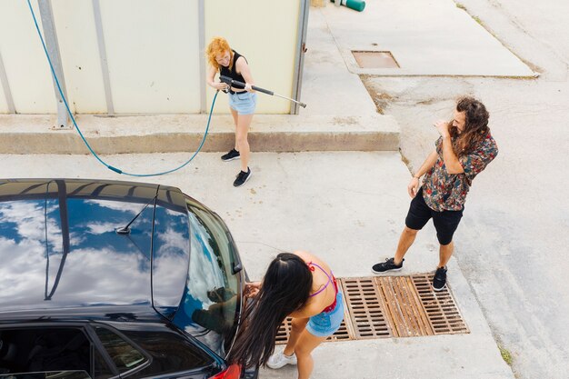 Mujer que salpica el agua en amigos en lavado de autos