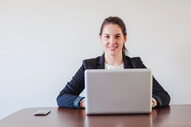 Mujer que se sienta en el escritorio que trabaja en la computadora portátil