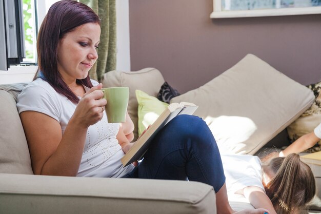 Mujer que se sienta en el sofá con la lectura de la taza