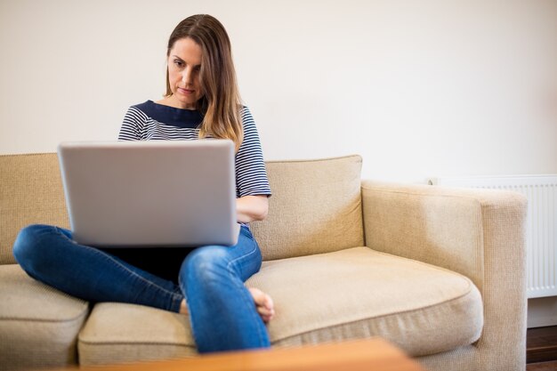 Mujer que se sienta en el sofá usando la computadora portátil en la sala de estar