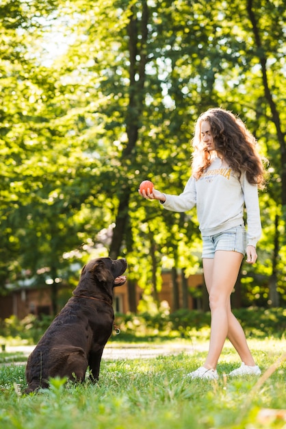 Mujer que sostiene la bola cerca de su perro en el parque