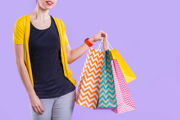 Mujer que sostiene el bolso de compras de papel colorido contra el papel pintado púrpura