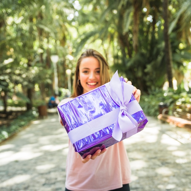 Mujer que sostiene la caja de regalo púrpura en el parque