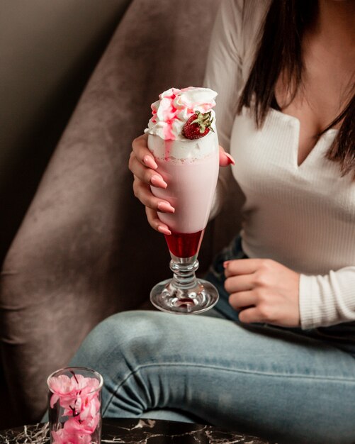 Mujer que sostiene un cóctel lechoso con jarabe de fresa y crema batida.