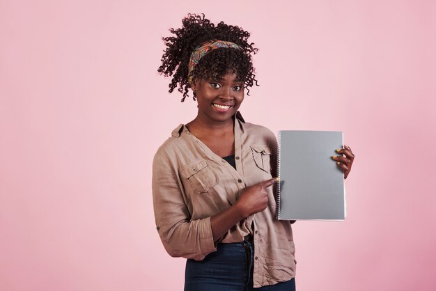 Mujer que sostiene el cuaderno gris en sus manos en el fondo rosado del estudio