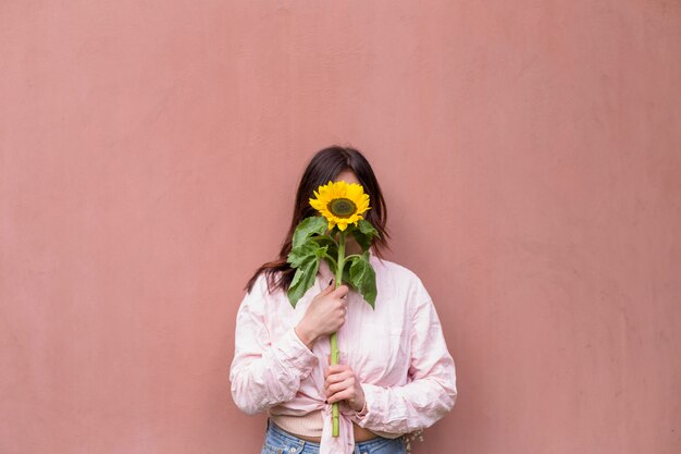 Mujer que sostiene la flor amarilla fresca cerca de la cara