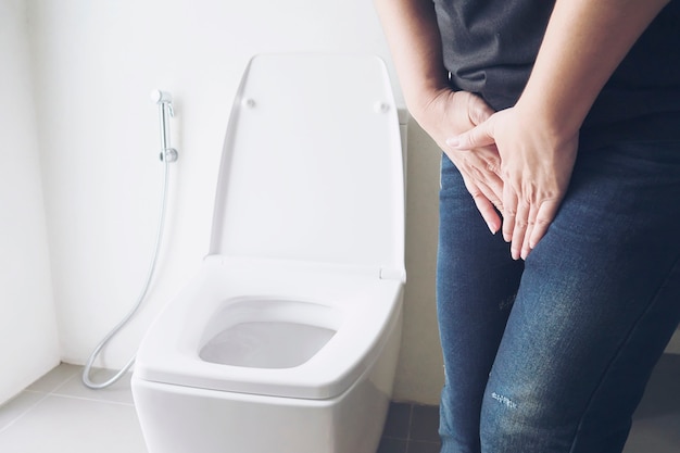 Mujer que sostiene la mano cerca de la taza del inodoro - concepto de problema de salud