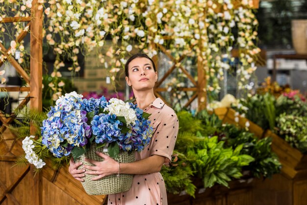 Mujer que sostiene la olla con flores en la casa verde