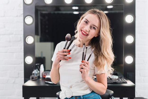 Mujer que sostiene pinceles de maquillaje en estudio