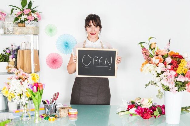 Mujer que sostiene la pizarra con palabra abierta chalkdrawn en tienda floral