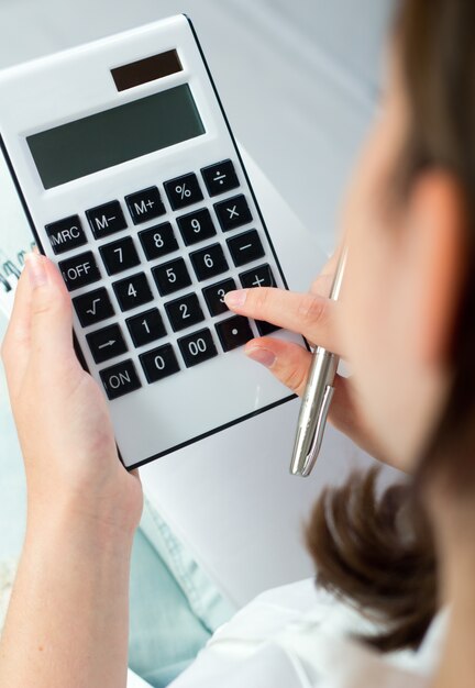 Mujer que sostiene la pluma y pulsando botones de la calculadora