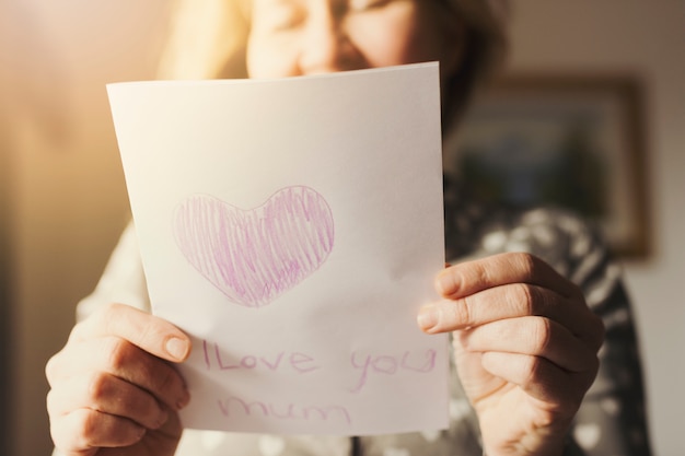 Mujer que sostiene la tarjeta de felicitación con te amo inscripción de mamá