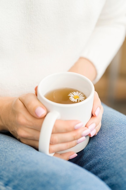 Mujer que sostiene la taza blanca con té y flores