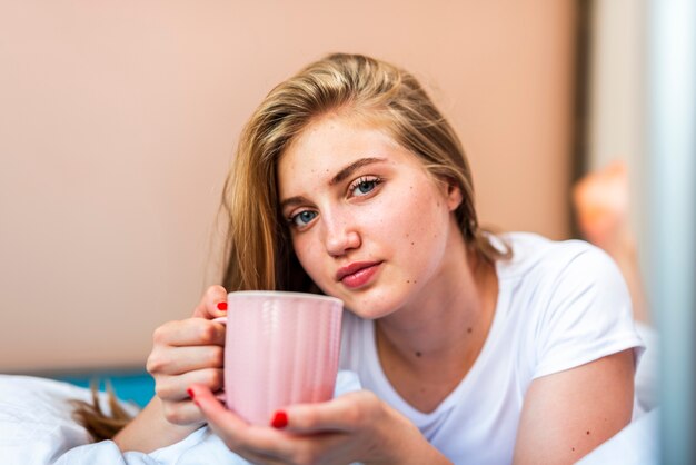 Mujer que sostiene la taza de café mientras está en la cama