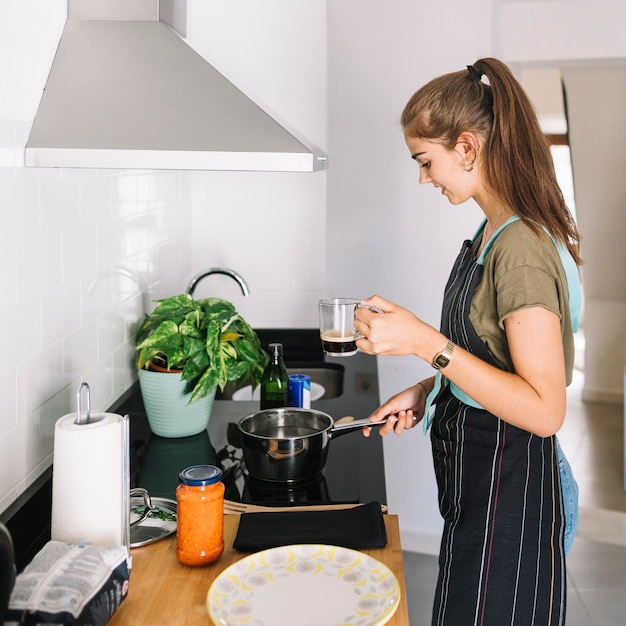 Mujer que sostiene la taza de café que prepara la comida en la cocina