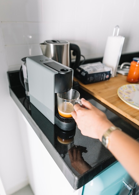 Mujer que sostiene la taza de cristal debajo de la máquina de café