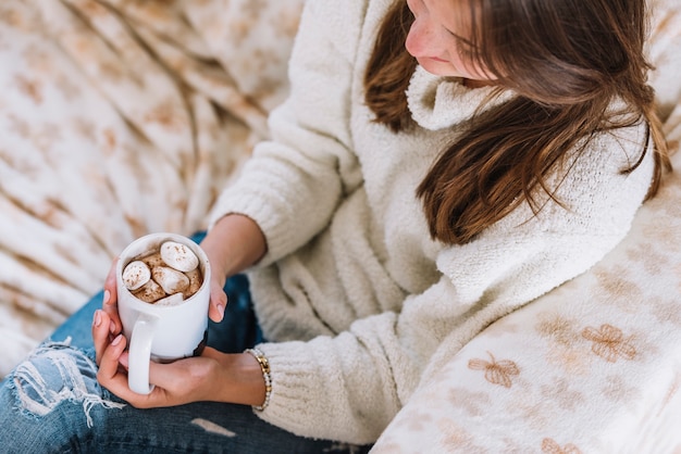 Mujer que sostiene la taza con malvaviscos en sofá