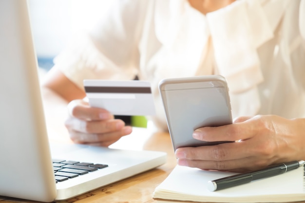 Mujer que sostiene el teléfono móvil y la tarjeta de crédito en la computadora portátil para las compras en línea