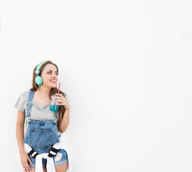 Mujer que sostiene el vaso de jugo con el auricular mirando lejos aislado sobre fondo blanco