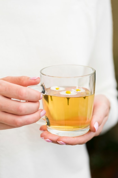 Mujer que sostiene el vidrio con té y flores