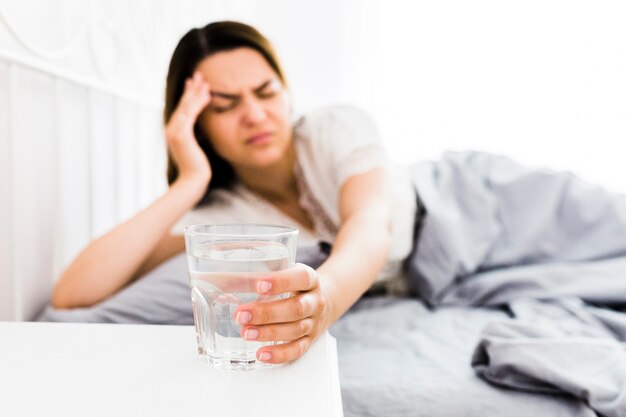 Mujer que sufre de dolor de cabeza tomando un vaso de agua