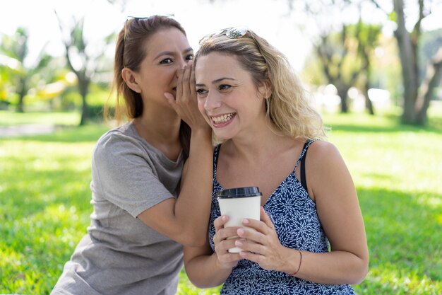 Mujer que susurra secreto a una amiga sonriente en el parque