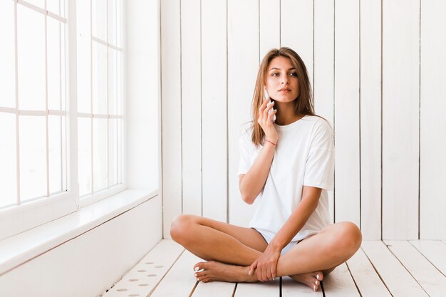 Mujer que tiene conversación telefónica junto a la ventana