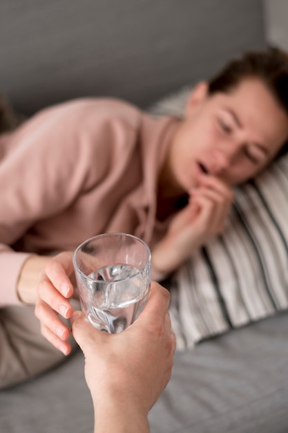 Mujer que tiene un resfriado recibiendo agua y pastillas