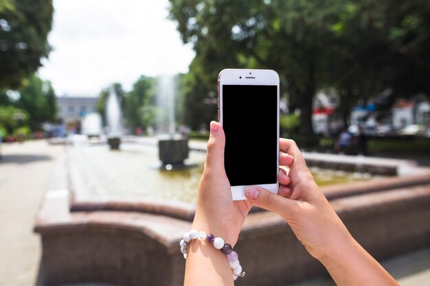 Una mujer que toma la imagen de la fuente a través del teléfono celular en el jardín