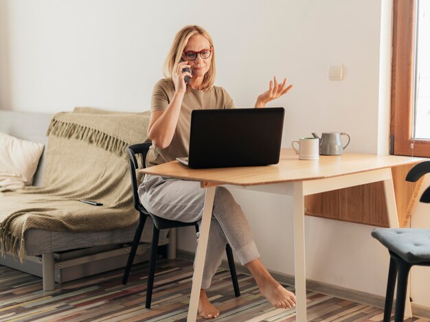 Mujer que trabaja en casa durante la cuarentena con computadora portátil y teléfono inteligente