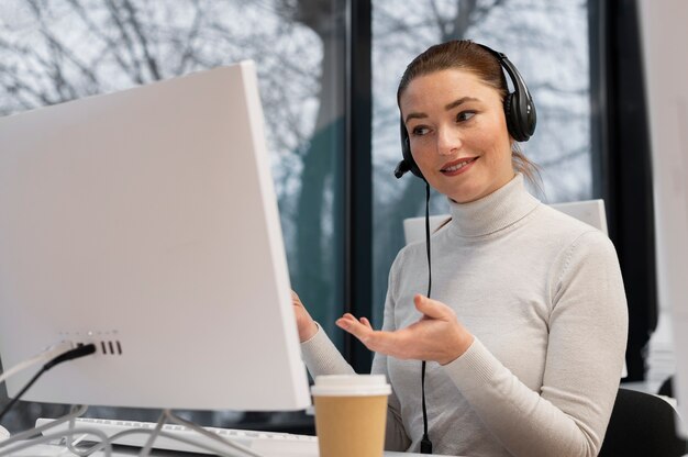 Mujer que trabaja en un centro de llamadas hablando con clientes usando auriculares y micrófono