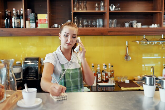 Mujer que trabaja como barista tomando orden telefónica