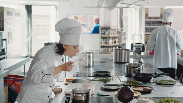 Mujer que trabaja como cocinera probando sopa mala para un plato gourmet, cometiendo un error al preparar una receta culinaria. Auténtico chef haciendo pruebas de sabor con salsa, cocinando en cocina gastronómica profesional.