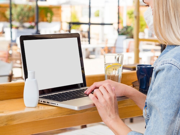 Mujer que trabaja en la computadora portátil al aire libre con desinfectante para manos