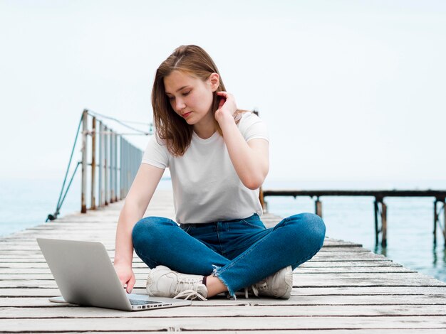 Mujer que trabaja en la computadora portátil al aire libre en el muelle