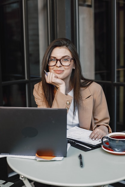 Mujer que trabaja en una computadora portátil en un café de la calle. Usar ropa elegante e inteligente: chaqueta, gafas