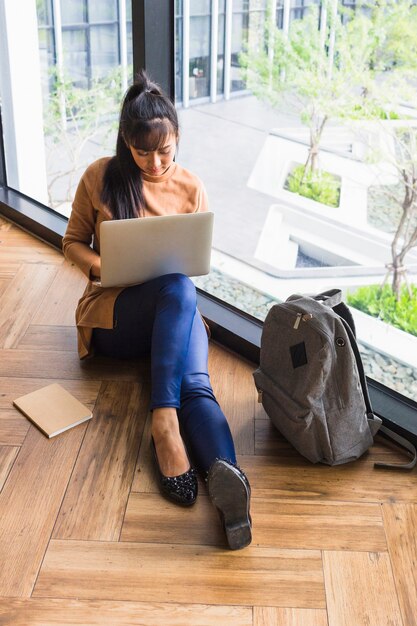 Mujer que trabaja en la computadora portátil cerca de la ventana