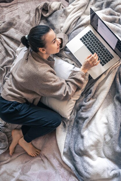 Una mujer que trabaja en una computadora portátil mientras está acostada en la vista superior de la cama