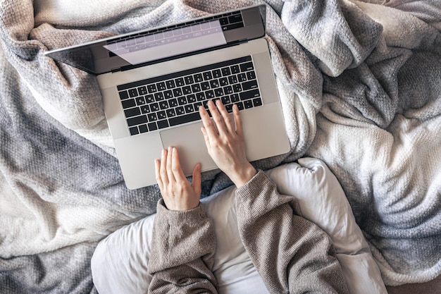 Una mujer que trabaja en una computadora portátil mientras está acostada en la vista superior de la cama