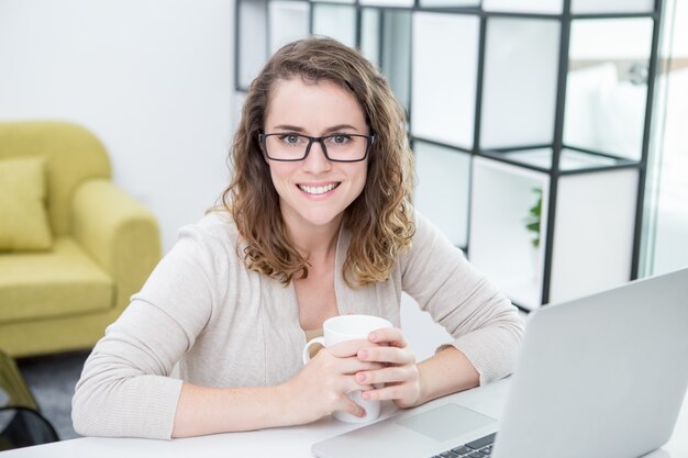 Mujer que trabaja en la computadora portátil y que bebe té en el país